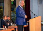 Innenminister Joachim Herrmann seitlich hinter Rednerpult, im Hintergrund zwei Personen am Tisch