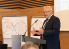 Herrmann am Rednerpult, im Hintergrund Skizzen an Flipcharts