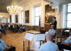 Kirchner am Rednerpult in königlichem Saal, im Vordergrund Musikkapelle, im Hintergrund Publikum