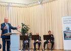 Herrmann am Rednerpult, im Hintergrund drei Musiker mit Instrument