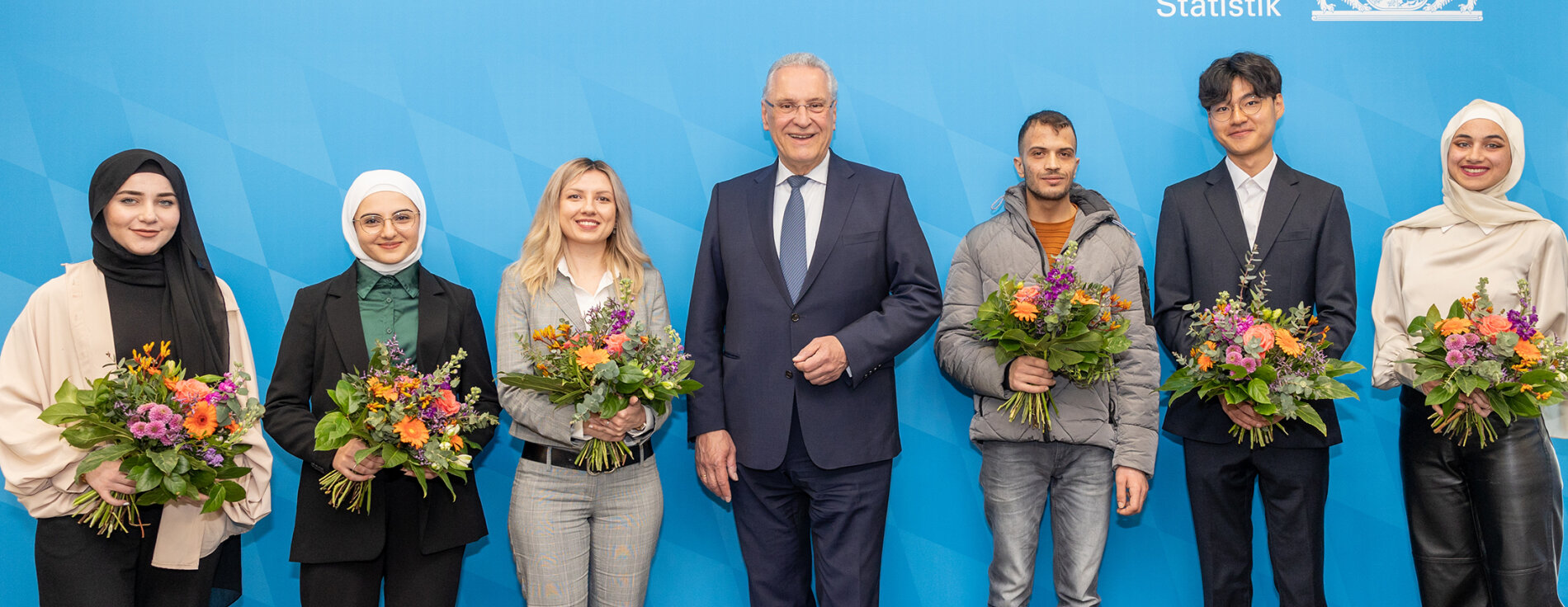 Gruppenfoto mit Innen- und Integrationsminister Joachim Herrmann in der Mitte, links und rechts neu Eingebürgerte mit Blumensträußen