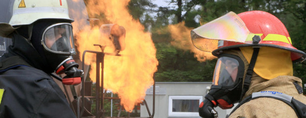 Zwei Feuerwehrleute. Dahinter ein großes Feuer.