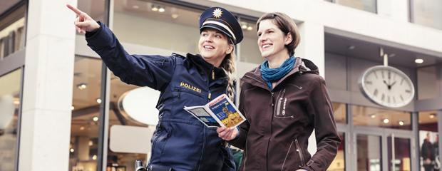 Eine uniformierte Polizistin zeigt einer Frau mit Reiseführer den Weg.